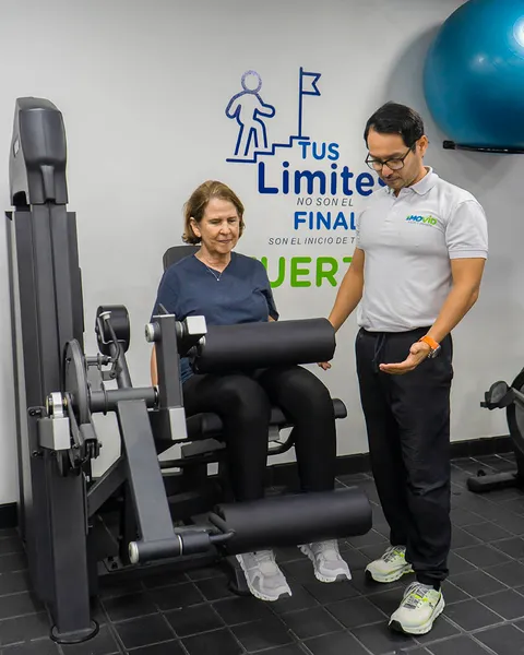Paciente adulto mayor en máquina de extensión de pierna con supervisión de un especialista MOVID